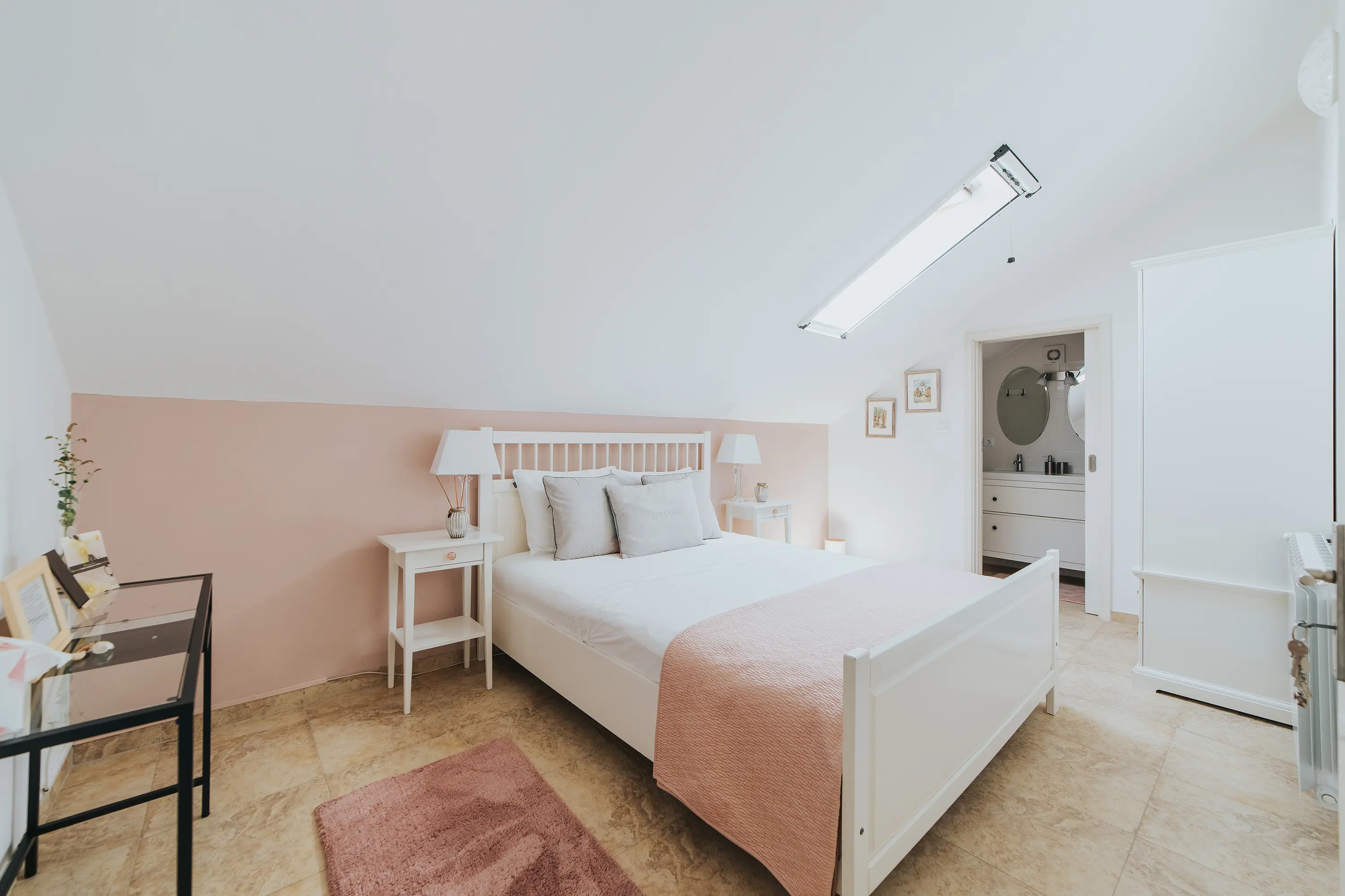 Fotografia de um quarto com bastante luz natural. Com uma mobília minimalista, é-lhe dado contraste com tons rosa. Um excelente exemplo de como um serviço profissional de fotografia de hotelaria irá impactar o seu espaço!